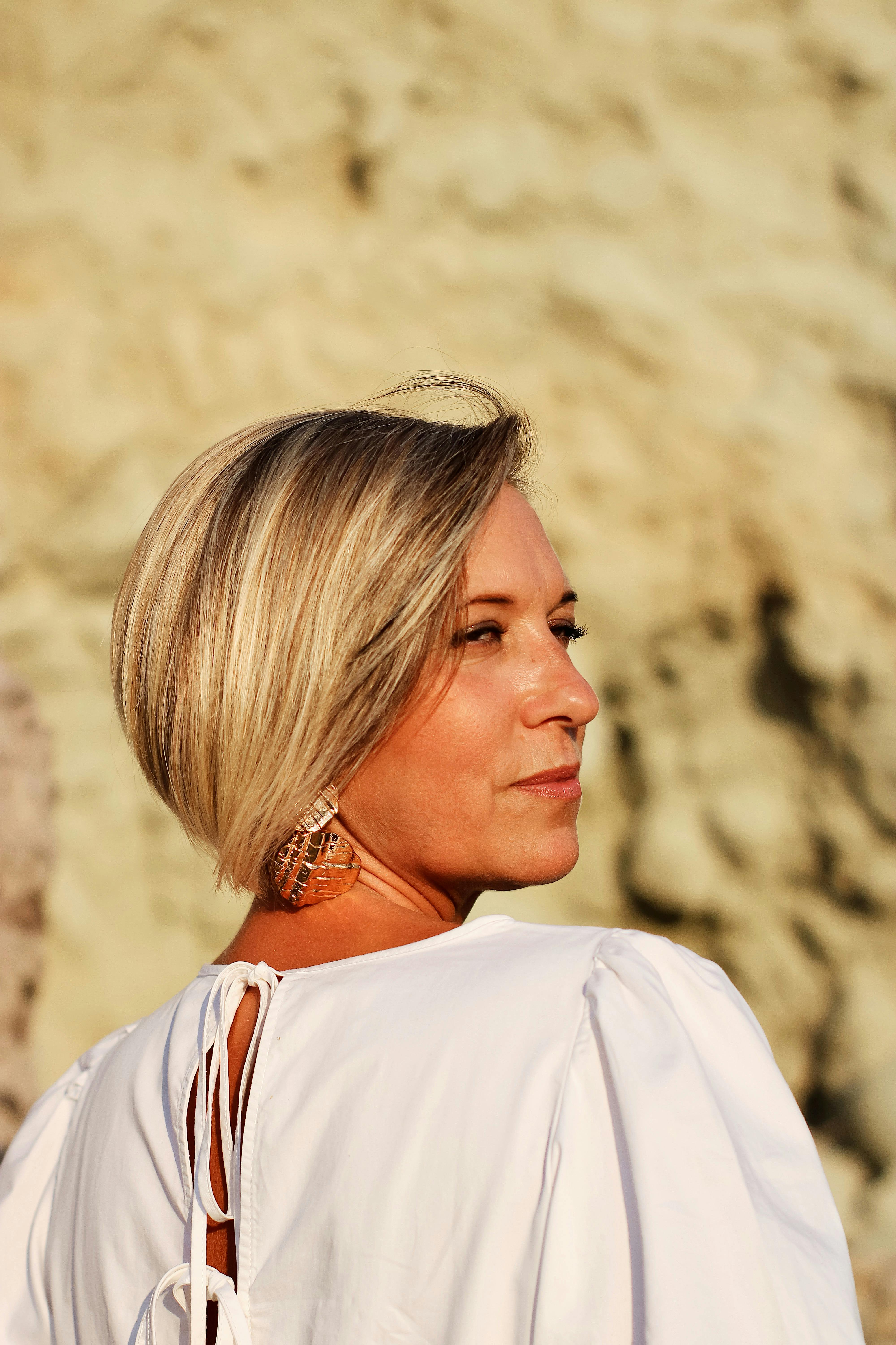 Middle-aged woman with short blonde hair gazing thoughtfully into the distance, standing outdoors in warm natural light