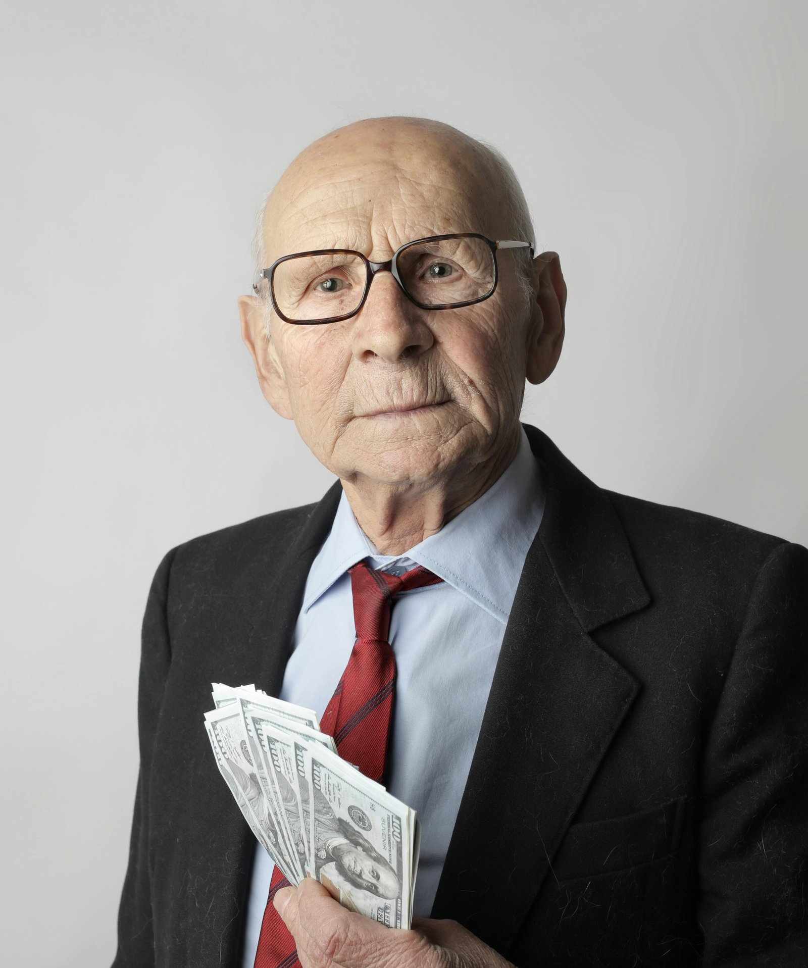 Older man wearing glasses and a suit holding cash in his hand, symbolizing finances, security, and money concerns in later life