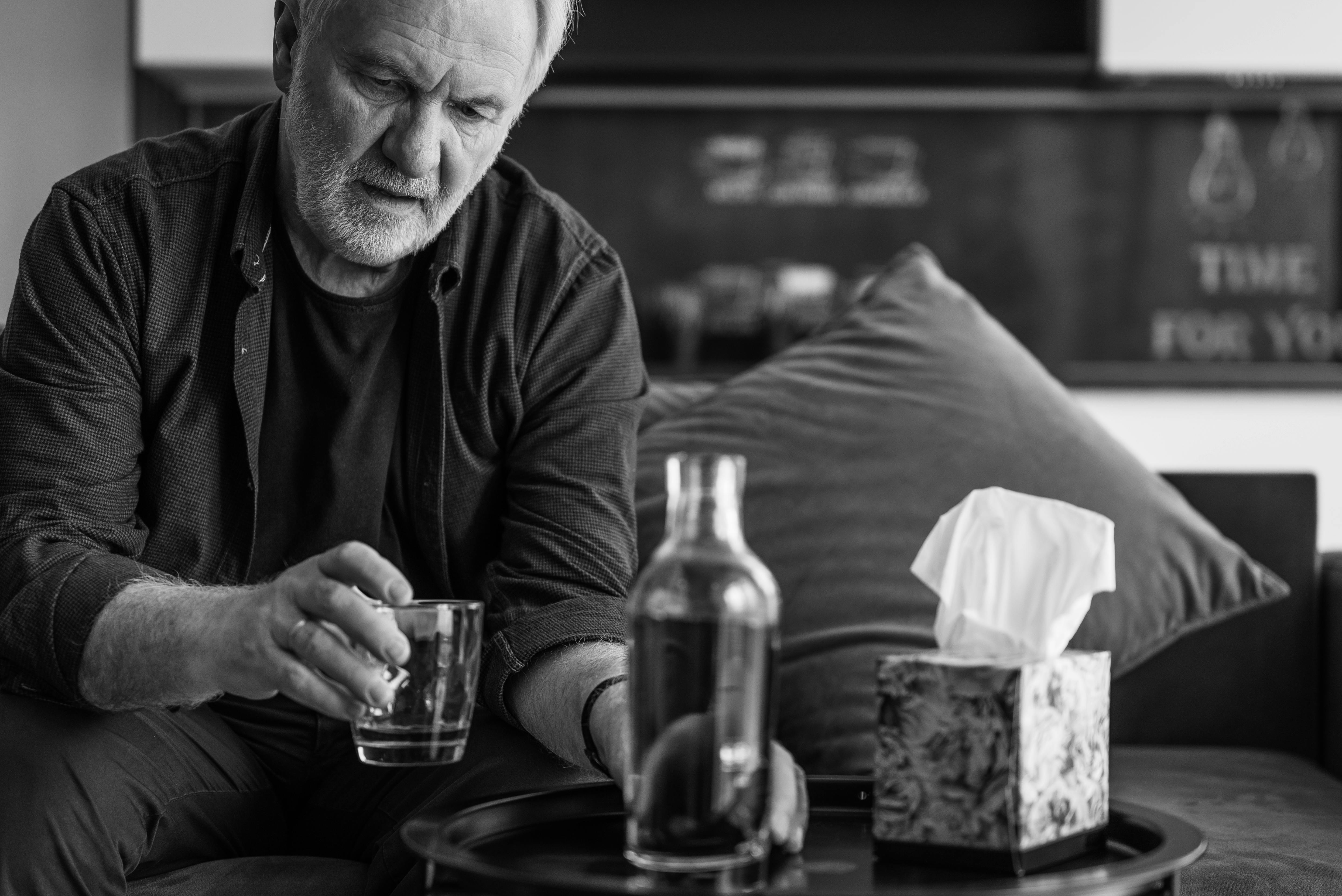 Older man sitting alone holding a glass, reflecting quietly in his living room