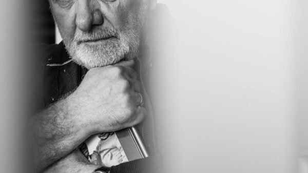 Close-up portrait of an older man holding a framed photo, deep in thought