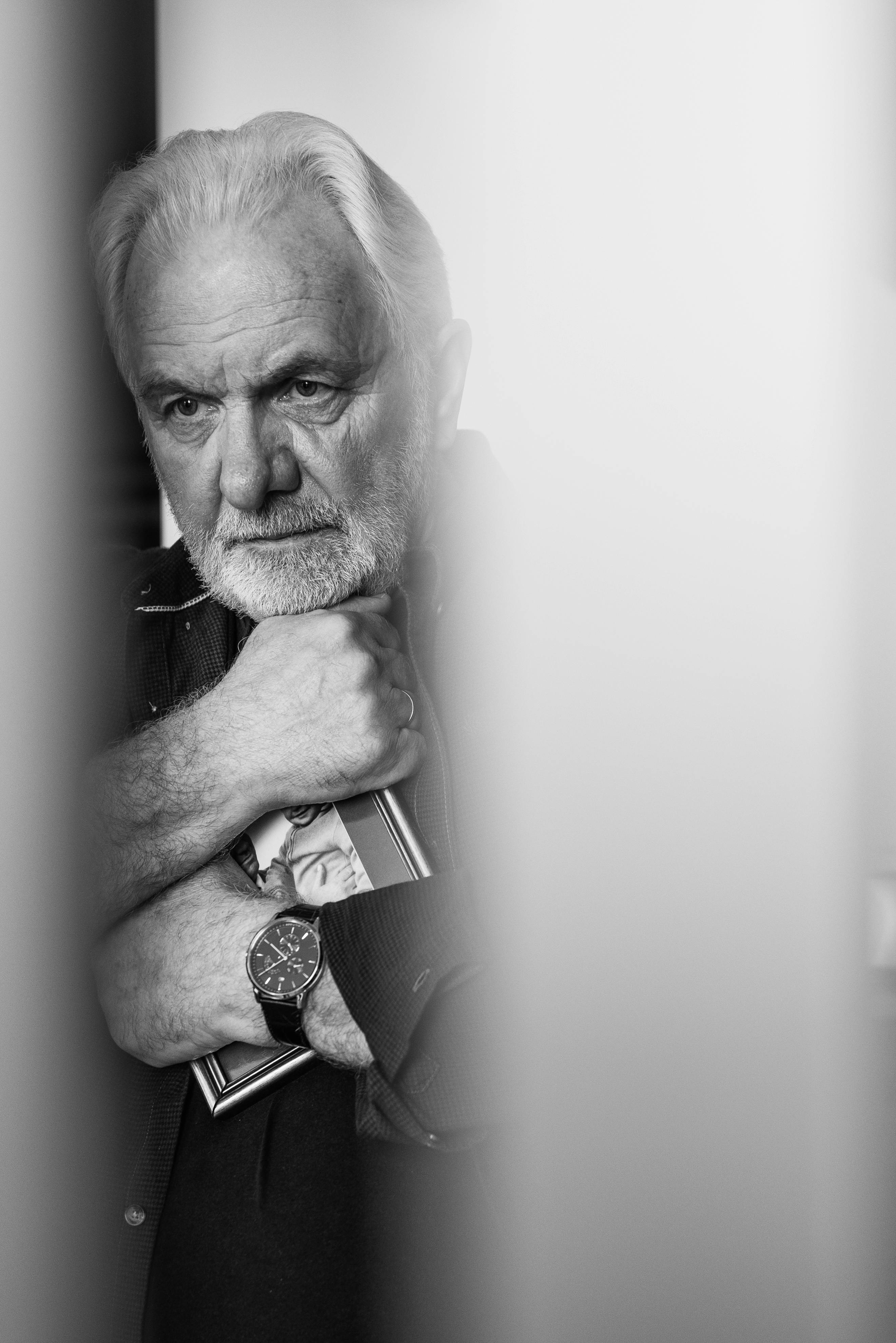 Close-up portrait of an older man holding a framed photo, deep in thought