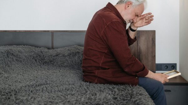 Older man sitting thoughtfully on a bed in a rustic room, reflecting quietly in natural light
