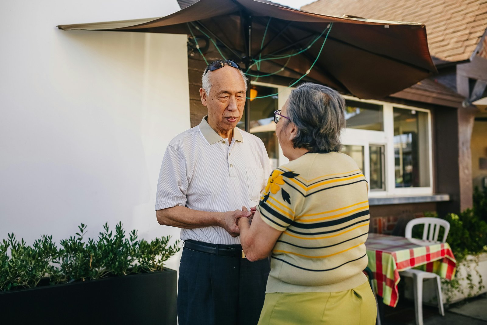 Elderly couple holding hands and talking outside a café, sharing a quiet emotional moment