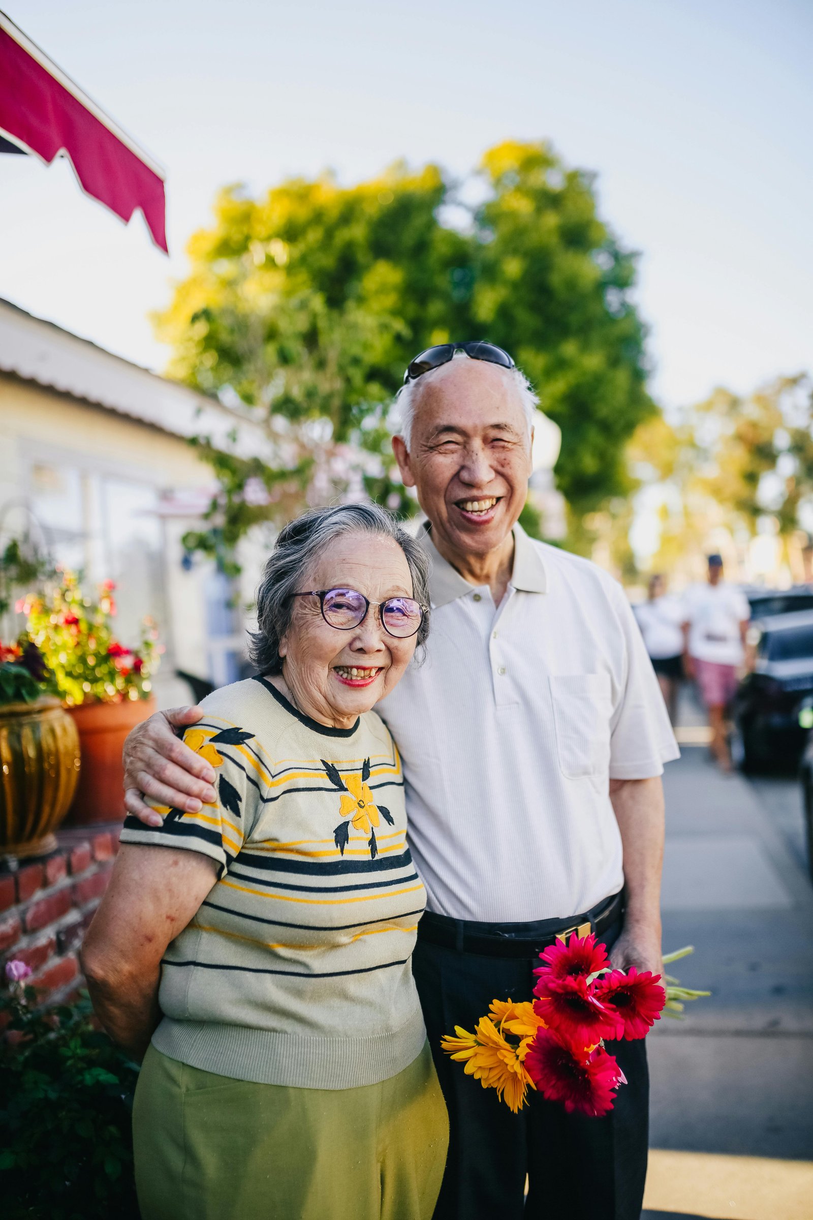 Smiling older couple standing together outdoors holding colorful flowers