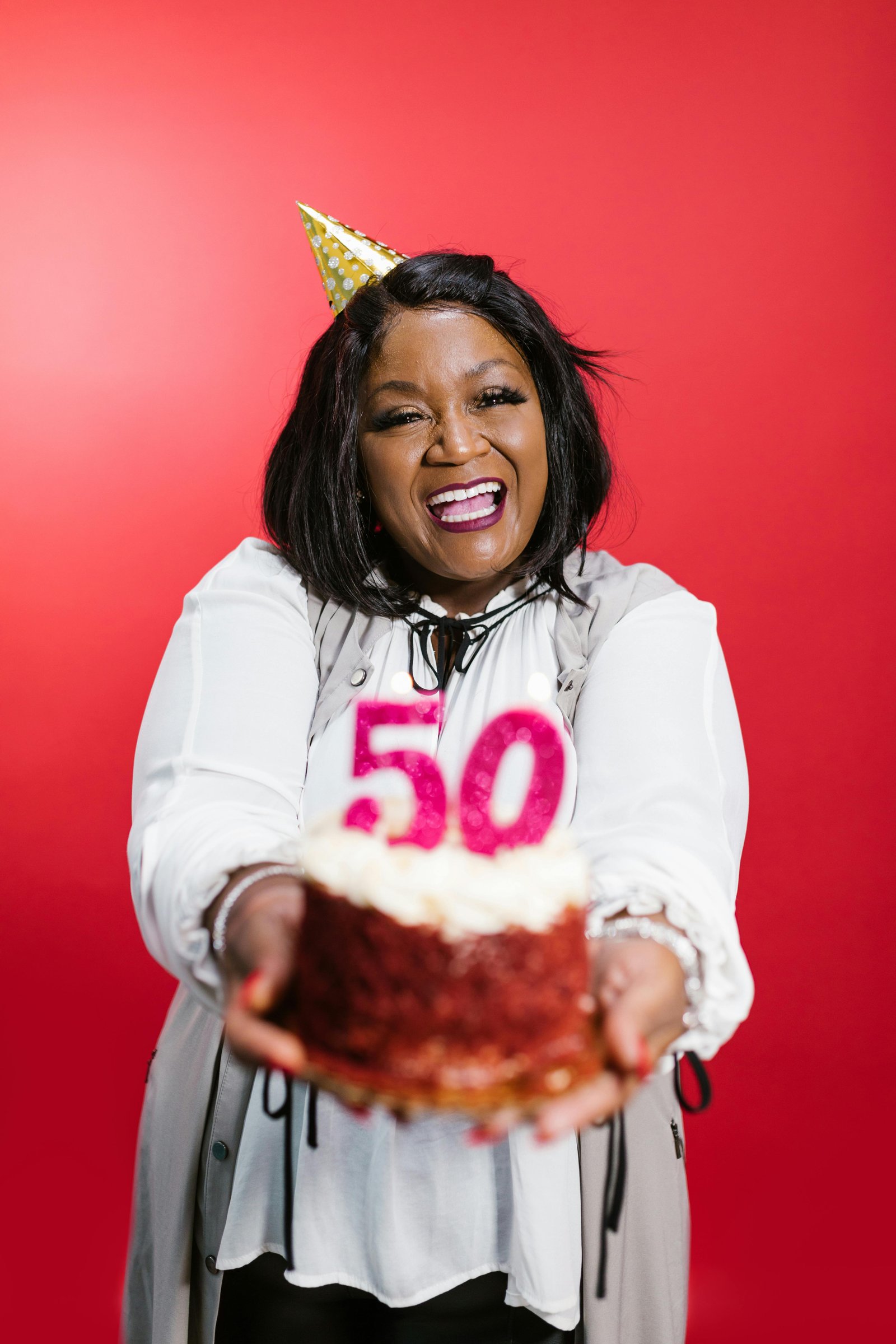 Smiling woman celebrating her 50th birthday while holding a cake with number 50 candles, symbolizing joy and confidence in midlife