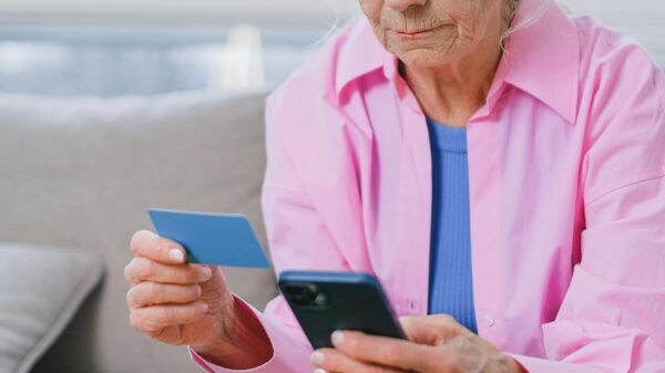 Older woman sitting on a couch holding a credit card and smartphone, focused on managing finances or making an online payment