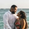 Couple standing by the ocean holding hands and smiling at each other, sharing a relaxed and affectionate moment by the water