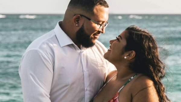 Couple standing by the ocean holding hands and smiling at each other, sharing a relaxed and affectionate moment by the water