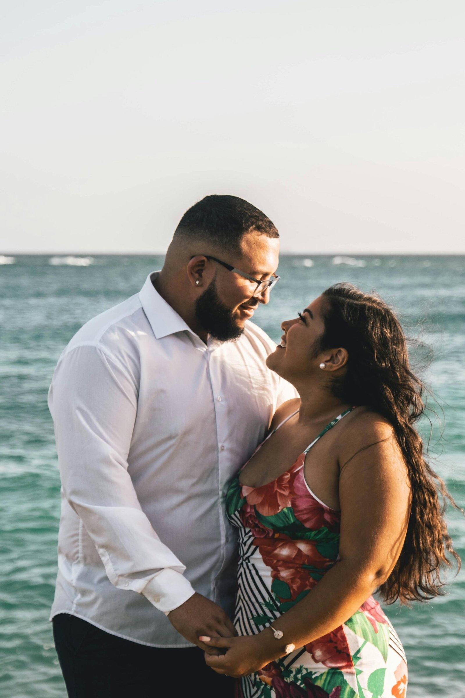 Couple standing by the ocean holding hands and smiling at each other, sharing a relaxed and affectionate moment by the water