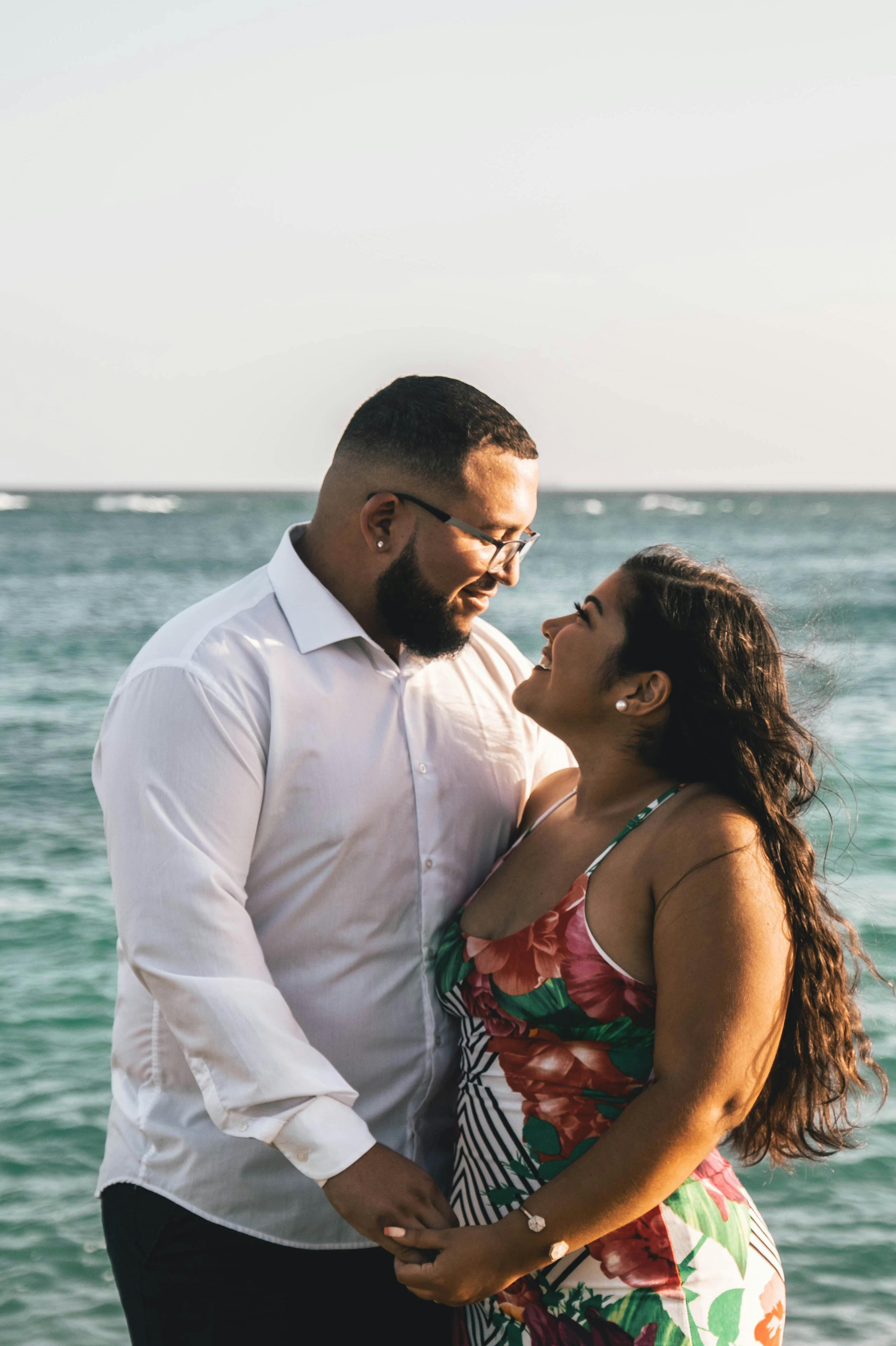 Couple standing by the ocean holding hands and smiling at each other, sharing a relaxed and affectionate moment by the water