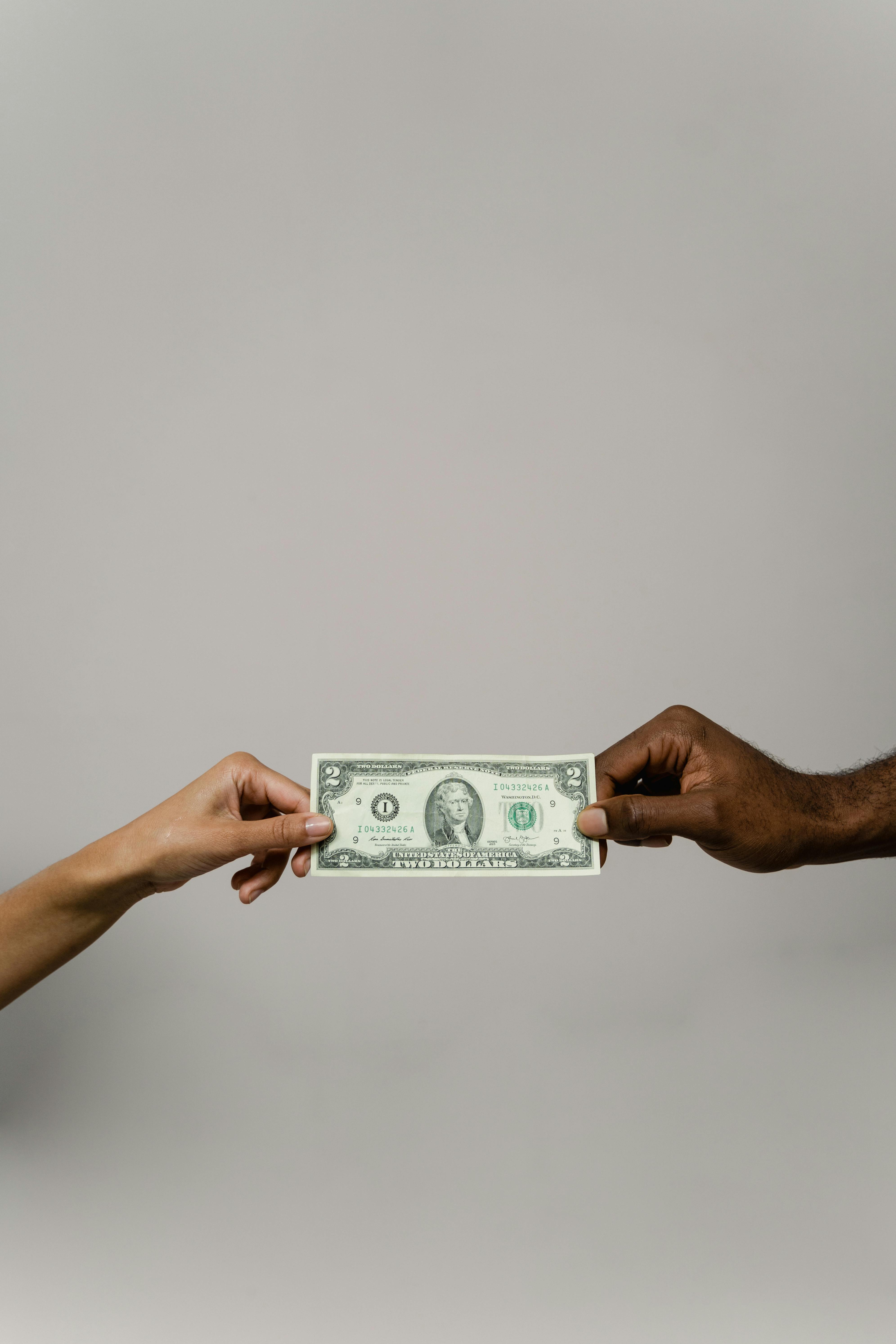 Two people exchanging a two-dollar bill, symbolizing financial decisions, trust, and emotional connections to money