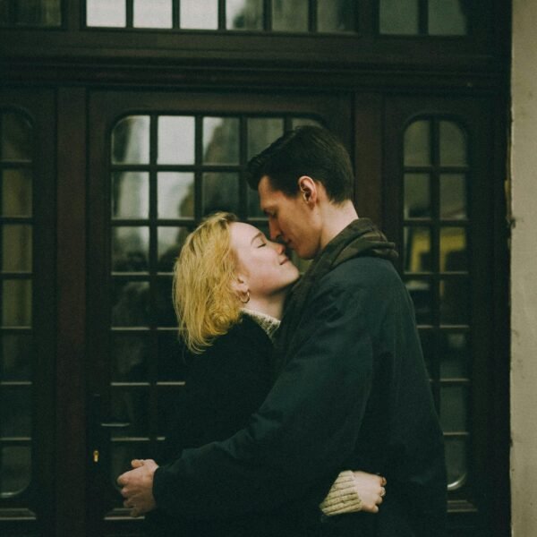 Couple embracing closely in front of a wooden doorway, sharing a quiet, intimate moment with eyes closed