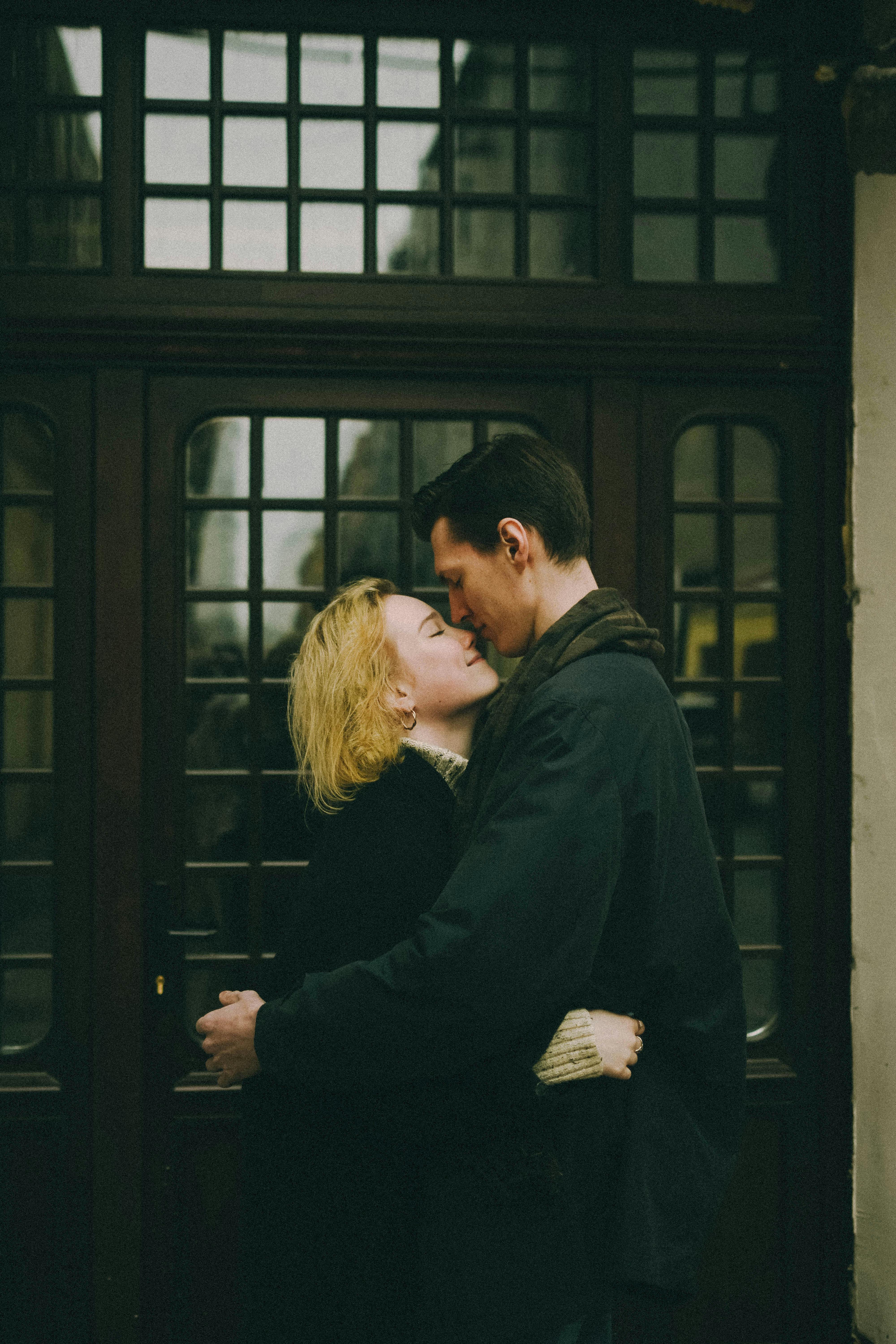 Couple embracing closely in front of a wooden doorway, sharing a quiet, intimate moment with eyes closed