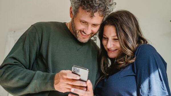 Midlife couple smiling together while looking at a phone, sharing a relaxed, intimate moment at home.
