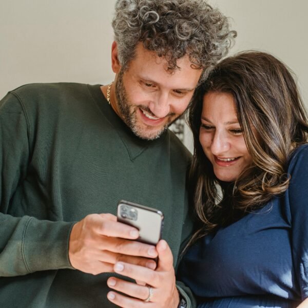 Midlife couple smiling together while looking at a phone, sharing a relaxed, intimate moment at home.