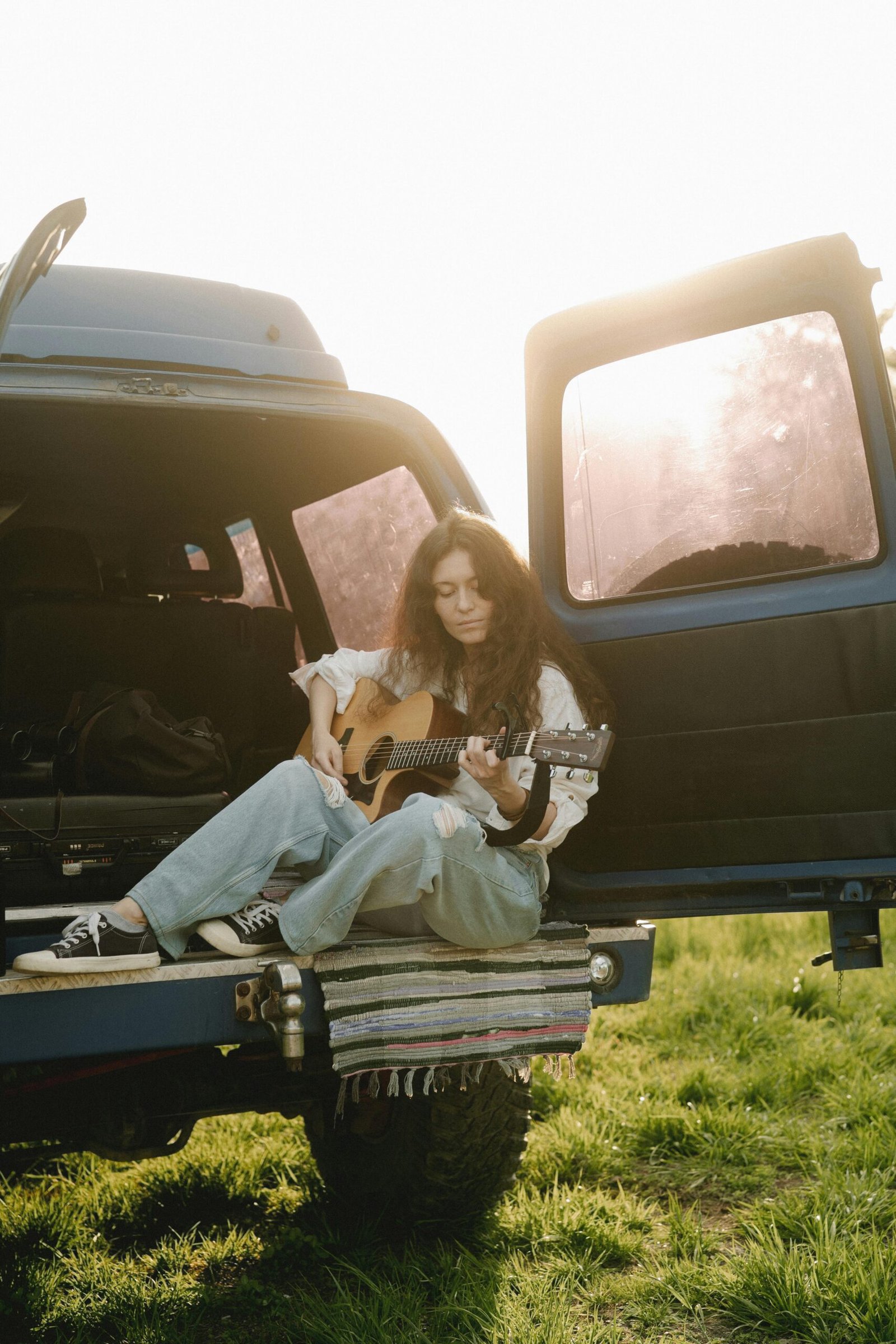 Woman playing guitar at the back of a van at sunset, embracing a creative second act in midlife
