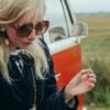 Woman in her 40s standing beside a vintage van, pausing thoughtfully while holding a cigarette during a reflective moment