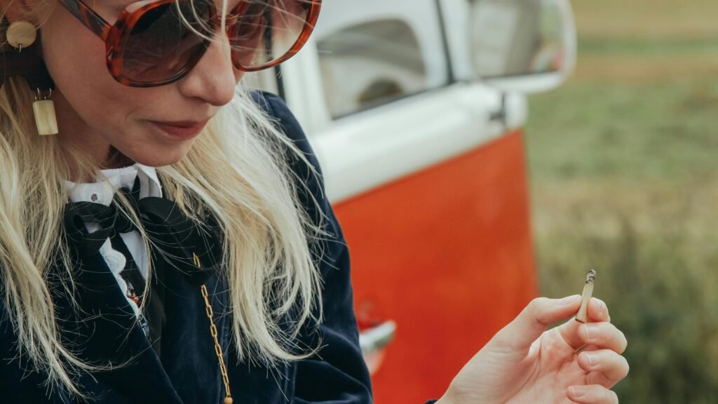 Woman in her 40s standing beside a vintage van, pausing thoughtfully while holding a cigarette during a reflective moment