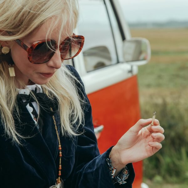 Woman in her 40s standing beside a vintage van, pausing thoughtfully while holding a cigarette during a reflective moment