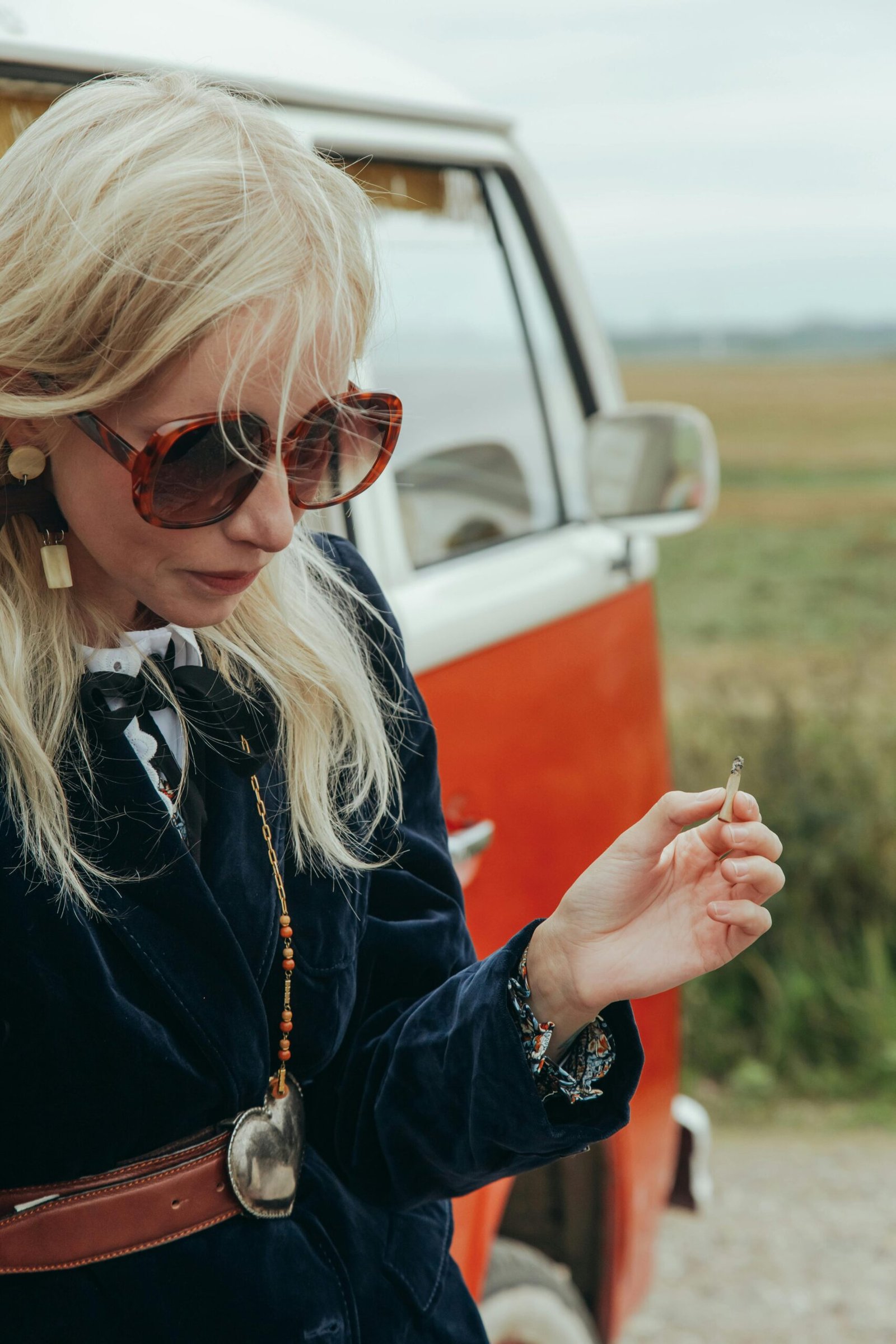 Woman in her 40s standing beside a vintage van, pausing thoughtfully while holding a cigarette during a reflective moment
