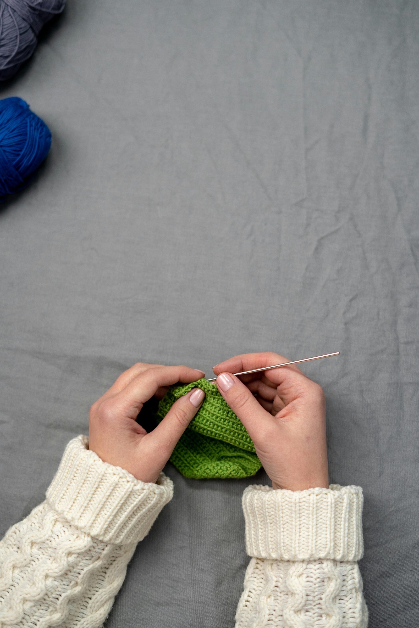 Hands crocheting a green fabric piece with yarn, representing a creative hobby becoming a second income