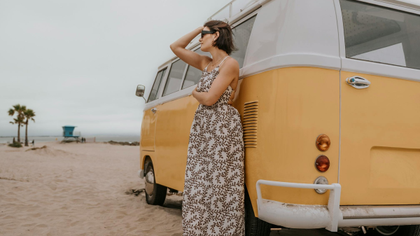 Woman standing beside a vintage van on the beach, pausing during a personal reinvention in midlife