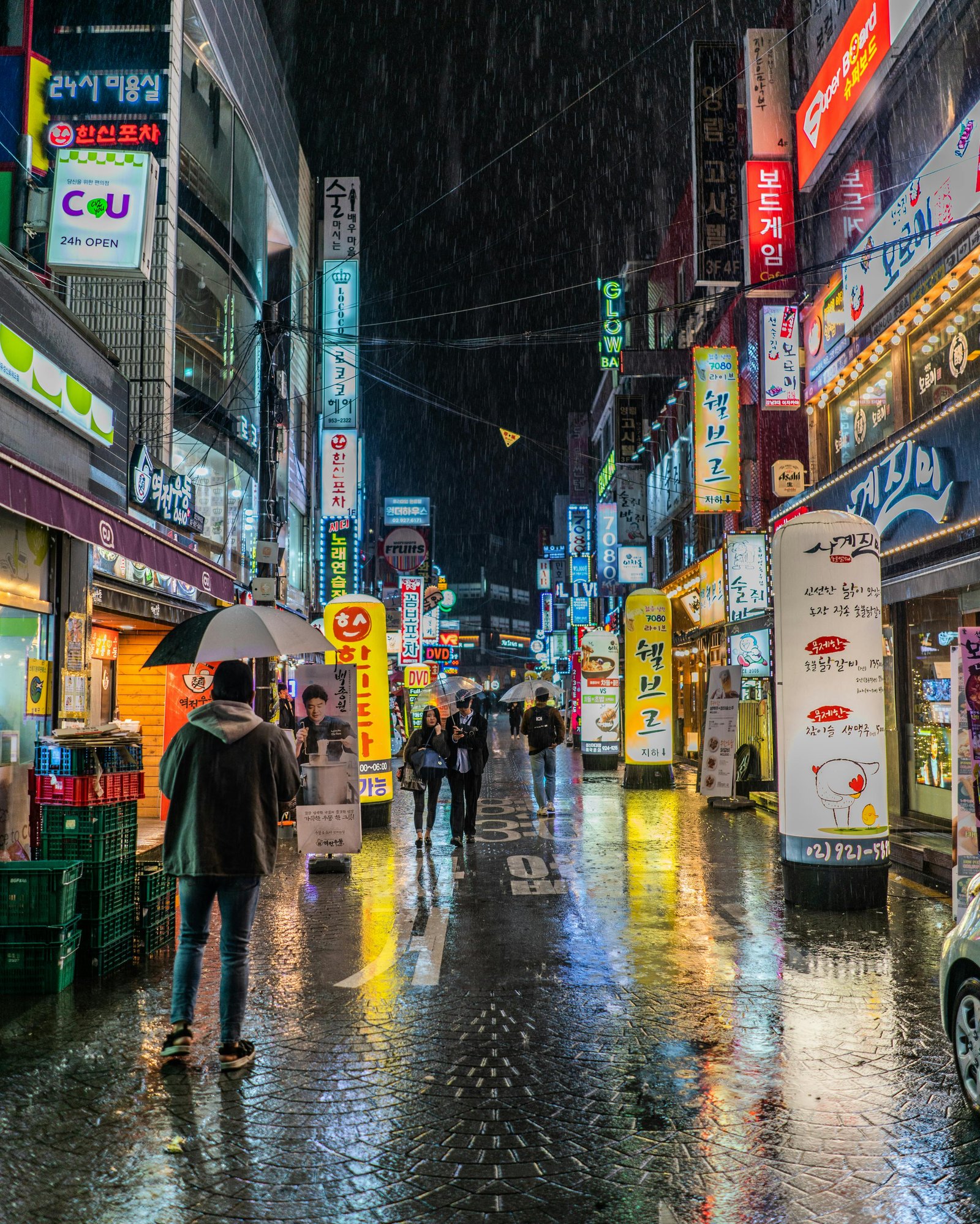 Rainy city street at night with neon signs and people walking under umbrellas