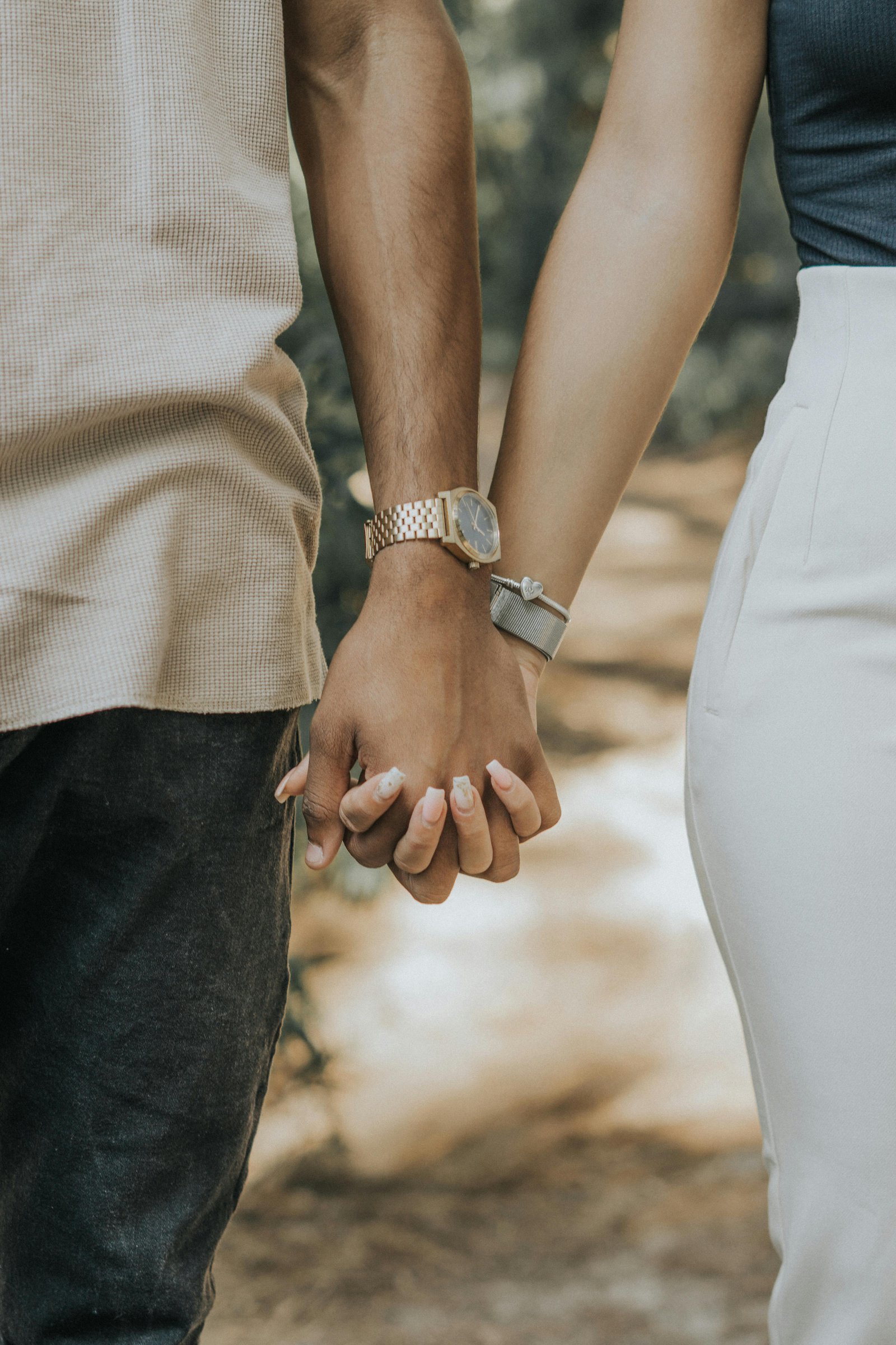 Close-up of a couple holding hands while walking outdoors, showing quiet intimacy and connection.