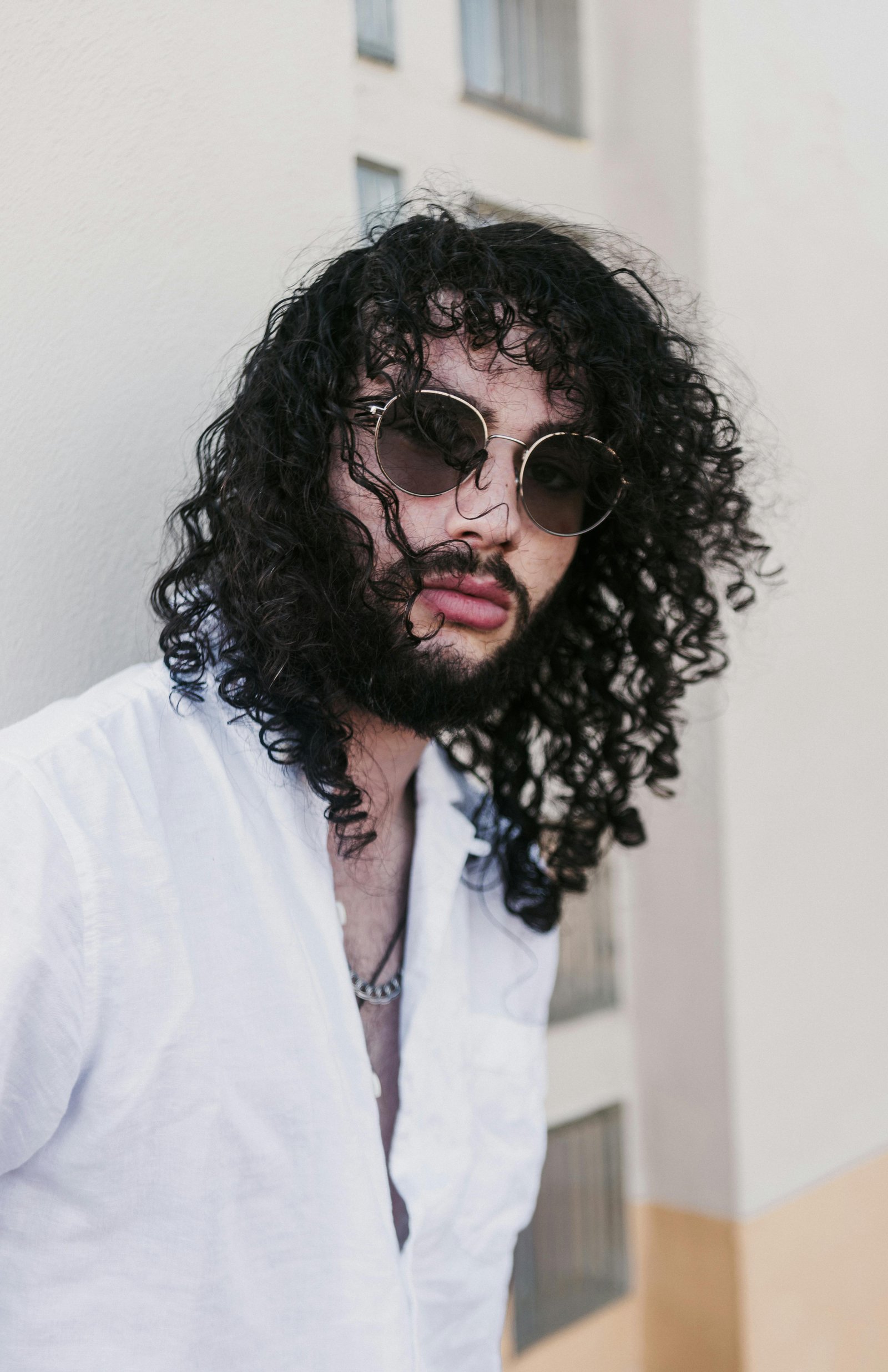 Curly-haired man in sunglasses reflecting quietly, expressing emotional awareness and self-expression in midlife
