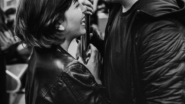 Black and white photo of a couple smiling at each other on a subway train